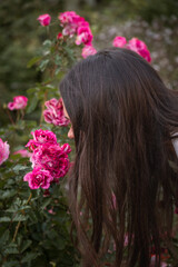 Naklejka premium Young woman smells pink roses in a garden, close-up portrait, soft daylight, rich green and pink tones, gentle and contemplative mood