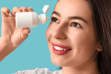 Young woman using eye drops on blue background, closeup