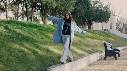 Young woman balances on edge of walkway in urban park during sunny day, wearing casual outfit and enjoying the outdoor setting © tol_u4f