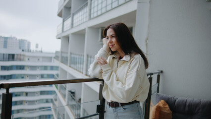 Woman stands on balcony and looks out at the view of the city on a cloudy day