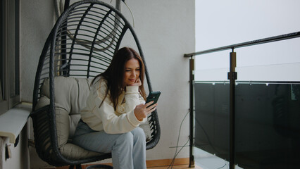 Relaxing on a balcony in a cozy hanging chair while using a smartphone to stay connected with friends and family during a quiet afternoon