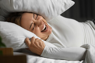 Angry mature woman with pillow screaming in bedroom at night. International Stress Awareness Week