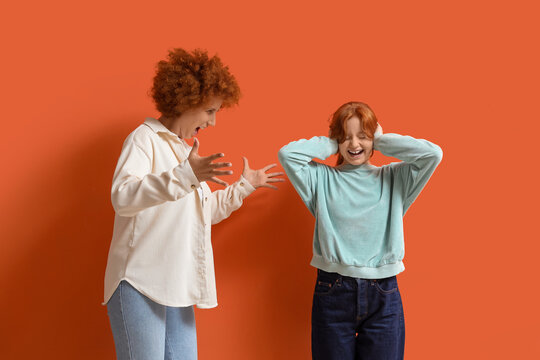 Redhead mother squabbling with her teenage daughter on orange background