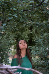 Naklejka premium Woman in a green sweater looks up beneath dense leafy branches, surrounded by deep green foliage and soft natural light, creating a calm mood