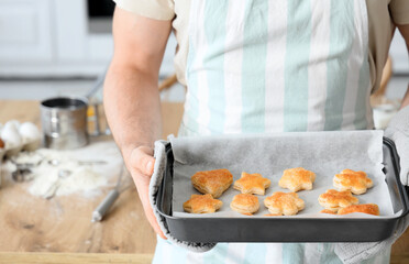 Young man with tasty cookies in baking pan at home