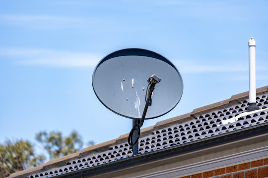 A satellite dish mounted on the tiled roof of a suburban house in Australia. Residential communication infrastructure, modern home technology, and rooftop installations