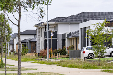 Quiet suburban street in Tarneit, Melbourne, lined with modern detached houses. Newly planted street trees, footpaths, and front gardens in a residential street in a growing outer suburb of Australia