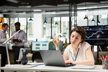 Obraz premium Pensive businesswoman playing with pen and contemplating over resource allocation in multinational company. Female manager focuses on laptop, evaluating budget funds and planning financial strategies.