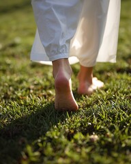 Bare feet walking on green grass under soft sunlight.