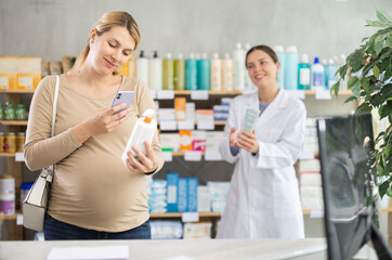 Pregnant woman scanning qr code for cream with woman pharmacist in pharmacy