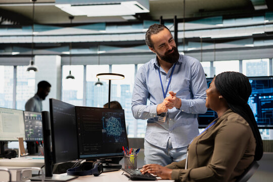 Pleased tech company manager applauding female programmer for optimizing code using AI. Satisfied team leader offering positive feedback to work done by african american woman in office - Powered by Adobe