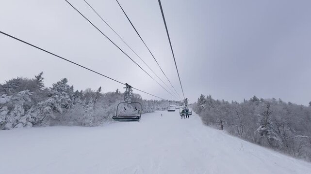 Ski chairlift at Killington Mountain, Vermont. Riding a lift in winter while snow skiing and snowboarding with white snowy trees and mountains. 4K video.