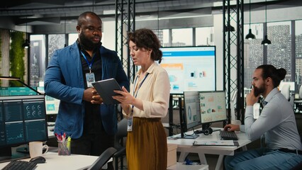 Obraz premium Two employees reviewing data insights on tablet in professional workspace, developing business solutions with strategy planning and performance metrics analysis for new goals achievement.