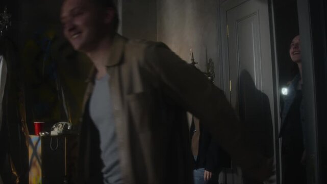 Medium shot group of young people opening door and entering abandoned house with flashlights exploring rooms , soft focus technique, copy space