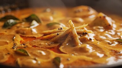 Captivating closeup of a rich aromatic Indian or Sri Lankan curry simmering vigorously in a traditional pan showcasing the vibrant colors and textures as a stream of flavorful red oil is expertly dri.