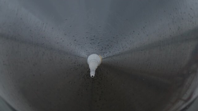 Extreme close up of military jet nose probe and fuselage surface with visible rain droplets during overcast weather