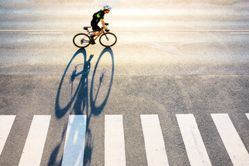 Bicyclist in motion with long shadow against asphalt
