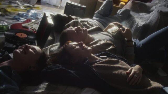 Candid close up shot of young people lying on floor in abandoned house and listening to music with retro record player all smiling, copy space