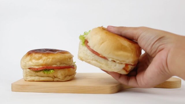 The hand takes a delicious hamburger that is on the cutting board pointing to the camera and then stacks another hamburger