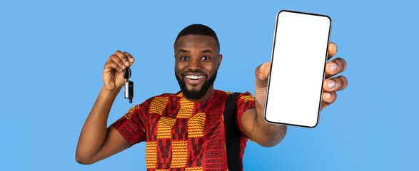 A young man smiles broadly while holding up a smartphone in one hand and car keys in the other. He...