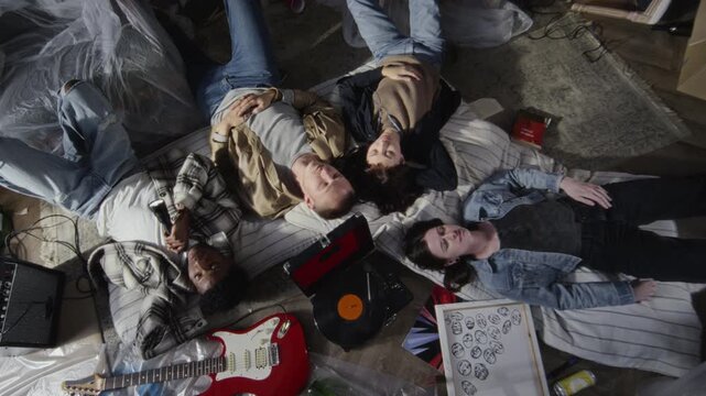 Top view shot of group of young people lying on floor in circle and listening to music with old record player while hanging out together in abandoned house, copy space