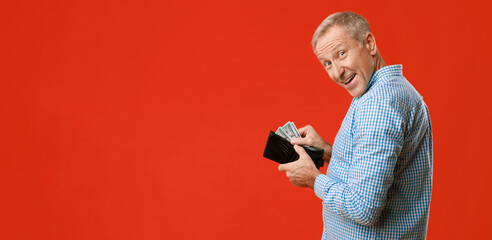 A man stands with a smile while taking cash out of a black wallet. He appears joyful, with a bright...