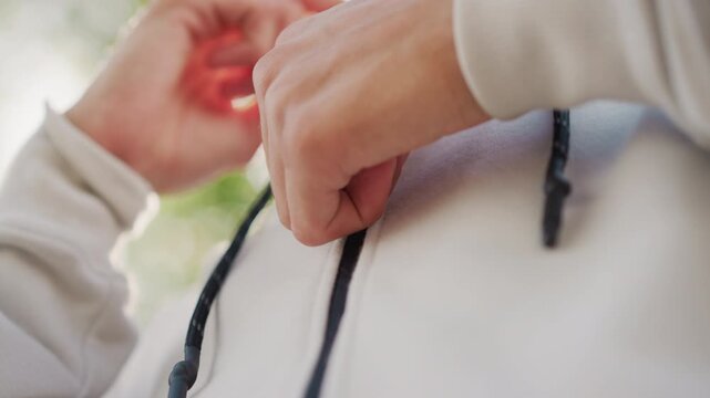hands adjusting hoodie drawstring near street in cloudy drizzle, closeup of torso and zipper with pocket and fleece texture visible, commuter preparing for light rain while walking through park lane
