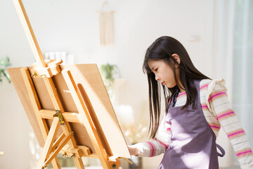 Young Asian girl painting with easel during creative activity at home