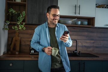 Man drinking coffee and checking phone in home office kitchen