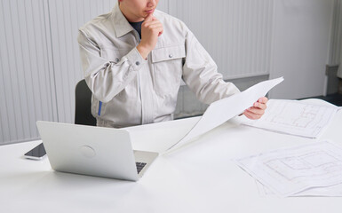 図面を持ってデスクで考える作業員　顔無し