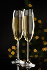 Merry Christmas and Happy New Year. Flute glasses with sparkling wine on black background against blurred lights