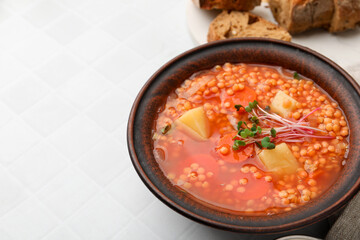 Tasty lentil soup in bowl on white tiled table, closeup. Space for text