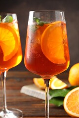 Glasses of refreshing spritzer cocktail and oranges on wooden table, closeup