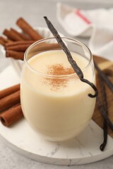 Delicious protein shake in glass, cinnamon and vanilla pods on table, closeup