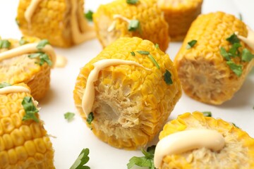 Pieces of boiled corn cobs with parsley and sauce on white table, closeup