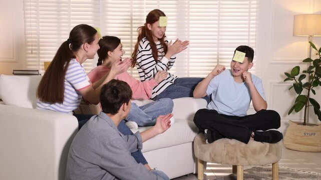 Group of teenage friends with sticky notes on their foreheads playing guess who game at home