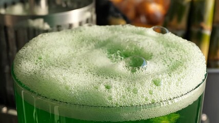 A vibrant and refreshing closeup shot of a bright green foamy beverage possibly a festive cocktail or a unique soda overflowing with a thick layer of bubbly froth in a clear glass perfect for celebra.