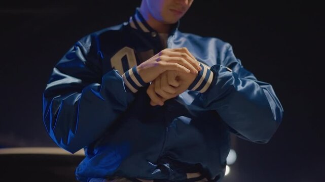 night street man checking watch, hands tense leaning on hood of parked car under neon lights adjusting varsity jacket and glancing at wrist, preparing to leave, cinematic closeups highlight texture,