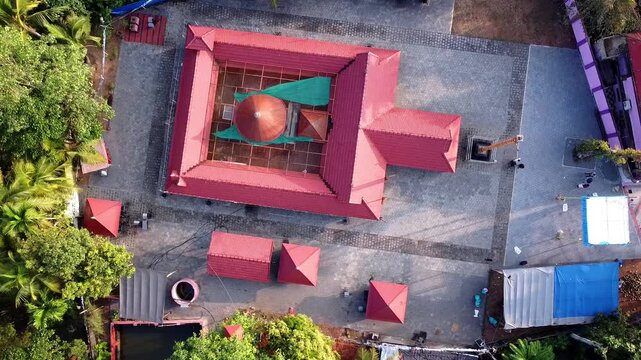 Top-down drone view of a traditional South Indian Hindu temple with red roofs and a central shrine (srikovil) in a paved courtyard surrounded by tropical trees.