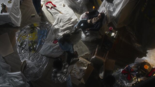 Top view shot group of young people with flashlights entering abandoned house and setting down on mattresses in secret hideout, soft focus technique, copy space