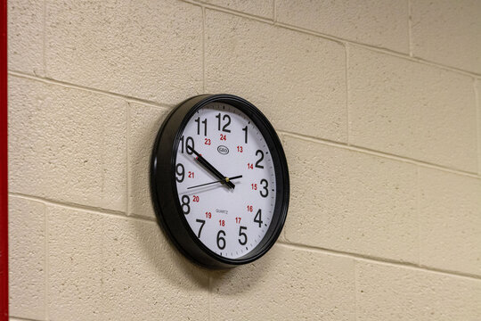 Canada, Quebec, 03 December 2025 : Black wall clock with numbers hangs on beige school hallway wall