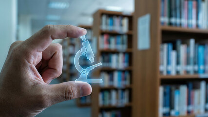 Hand holding translucent microscope icon in library suggesting scientific research and learning curiosity