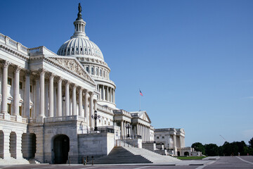 United States Capitol building with iconic dome and American flag under clear blue sky in...