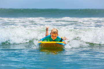 Happy young surfer boy with bodyboard have fun on beach, riding on small ocean waves. Summer adventures, active families, parents and kids lifestyle, sports activities on school holiday with kids