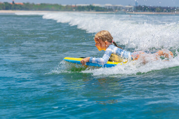 Happy young surfer girl with bodyboard have fun on beach, riding on small ocean waves. Summer adventures, active families, parents and kids lifestyle, sports activities on school holiday with kids