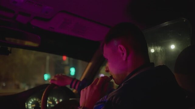 white man driving through neon intersection, hand near mouth, cigarette and smoke, dashboard lights and stoplights changing, portrayed as oncall courier, nightshift worker, lone cab driver