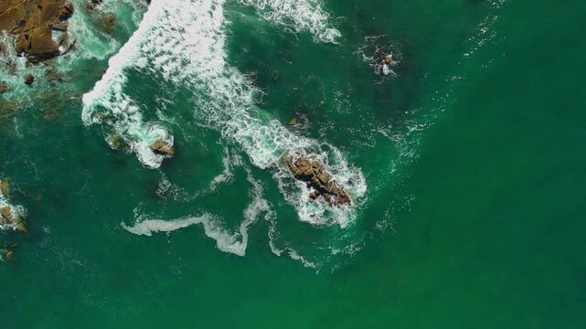 Aerial drone hovering birds-eye view rising above ocean waves crashing against coastal rocks in Portugal