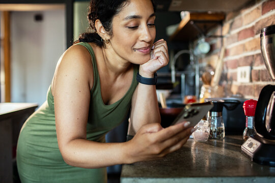 Adult woman checking smartphone with relaxed smile in home kitchen