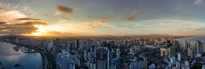 Expansive panoramic drone shot of Panama City's coastline and skyline bathed in warm golden sunset...