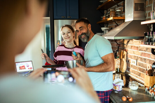 Mature father and teen daughter smiling while baking in home kitchen